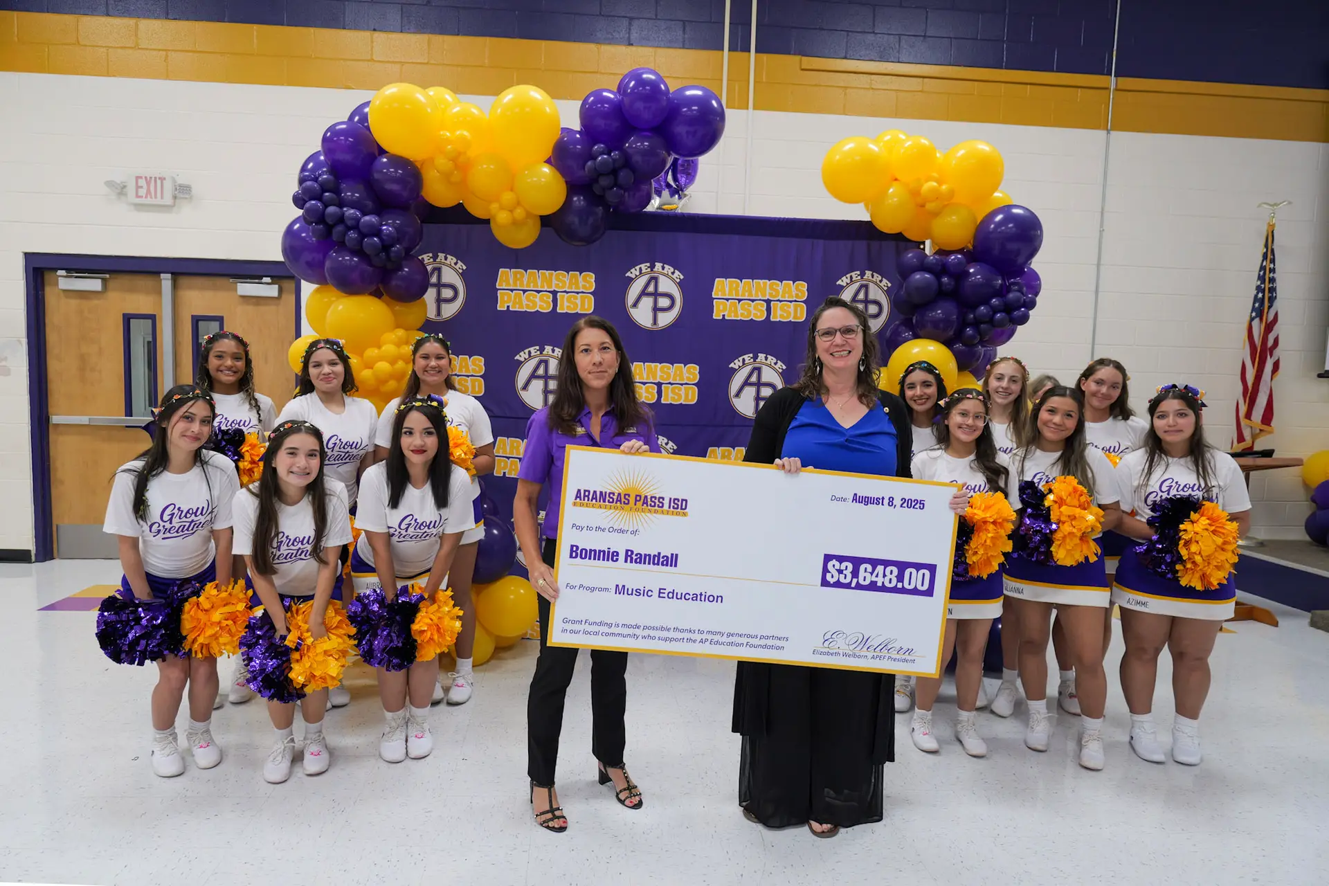 Mrs. Randall is awarded $3648.00 for music education. She is holding the award with an Education Foundation member, and they are surrounded by the high school varsity cheerleaders